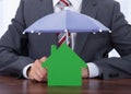 Businessman Sheltering House With Umbrella