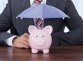Businessman sheltering piggybank with umbrella at desk