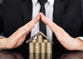 Businessman Shielding House Made Of Money At Desk Royalty Free Stock Photo