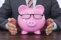 Businessman Shielding Piggybank Wearing Glasses