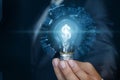 Businessman showing light bulb with burning dollar hologram inside on blue background