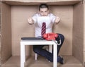 Businessman showing a protective mask, sitting in his little cardboard office