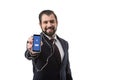 Bearded businessman with earphones showing smartphone with facebook website