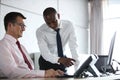 Businessman showing something to male colleague on laptop at office desk Royalty Free Stock Photo