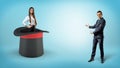 A businessman shows a self-assured businesswoman standing inside a giant illusionists hat on a blue background.