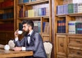 Businessman sits in vintage interior, holds book and cup of tea. Bearded man in luxury suit in his cabinet. Mature man with calm f Royalty Free Stock Photo