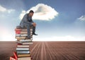 Businessman sitting on Books stacked by blue cloudy sky Royalty Free Stock Photo