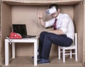 Businessman sitting in a cramped cardboard office, virtual glasses on his head, finger in the air, copy space