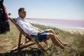 Businessman sitting in deck chair at beach of pink sea on sunny day. Royalty Free Stock Photo