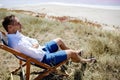 Businessman sitting in deck chair at beach of pink sea on sunny day. Royalty Free Stock Photo