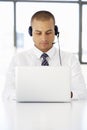 Businessman Sitting At Desk In Office Using Laptop Wearing Headset Royalty Free Stock Photo