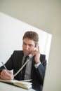 Businessman sitting at his office desk talking on white landline phone and making notes Royalty Free Stock Photo