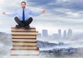 Businessman sitting meditating on Books stacked by distant city Royalty Free Stock Photo