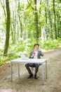 Businessman sitting at the office desk with laptop computer and cup of coffee talking mobile phone on in green forest park. Busine Royalty Free Stock Photo