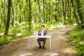 Businessman sitting at the office desk with laptop computer and cup of coffee talking mobile phone in green forest park. Business Royalty Free Stock Photo