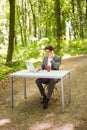 Businessman sitting at the office desk with laptop computer and cup of coffee talking mobile phone in green forest park. Business Royalty Free Stock Photo