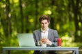 Businessman sitting at the office desk work at laptop computer and cup of coffee tuping on mobile phone on road of green forest pa Royalty Free Stock Photo