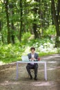 Businessman sitting at the office desk work at laptop computer and cup of coffee typing mobile phone on road of green forest park. Royalty Free Stock Photo