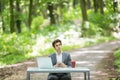 Businessman sitting at the office desk work at laptop computer and cup of coffee typing mobile phone on road of green forest park. Royalty Free Stock Photo