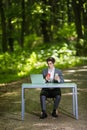 Businessman sitting at the office desk work at laptop computer and cup of coffee use mobile phone on road of green forest park. Bu Royalty Free Stock Photo