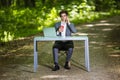 Businessman sitting at the office desk work at laptop computer and cup of coffee use mobile phone on road of green forest park. Bu Royalty Free Stock Photo