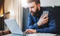 Businessman sitting in office at table,typing on laptop, holding smartphone.Man works on computer, analyzes information. Royalty Free Stock Photo