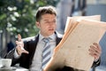 Businessman sitting outdoors having coffee cup for breakfast early morning reading newspaper news looking upset Royalty Free Stock Photo