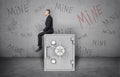 Businessman sitting on safe and background of wall with inscription `Mine`.