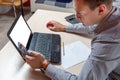 Businessman sitting at the table with a laptop in the office and looking tensely into the phone Royalty Free Stock Photo