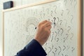 Businessman sketching many question marks on office whiteboard