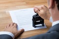 Businessman Stamping Contract Document At Desk