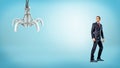 A businessman standing on blue background half-turned to look at a metallic robotic hand. Royalty Free Stock Photo