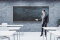 Businessman standing in classroom interior with empty blackboard Royalty Free Stock Photo