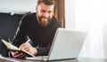 Businessman is standing by computer, looking at laptop screen, making notes in notebook. Man watching webinar, learning. Royalty Free Stock Photo