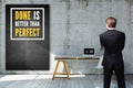 Businessman standing in front of a chalkboard with a message `Done is better than perfect`