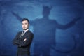 Businessman standing with hands across and his shadow on blue blackboard behind him tail like devil