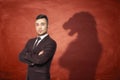 Businessman standing with hands across and his shadow on red empty blackboard behind looking like lion