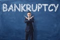 Businessman standing with his hands like cross sign and word `Bankruptcy` written on blackboard behind him