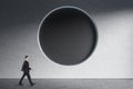 Businessman standing in minimalistic concrete interior with abstract clean black round poster on wall. Mock up. Exhibition, Royalty Free Stock Photo