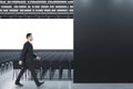 Businessman standing in modern grey auditorium with seating, empty screen and mock up place for your advertisement. Show premiere Royalty Free Stock Photo