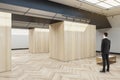 Businessman standing in modern wooden exhibition hall interior with sunlight from ceiling window, mock up place and seats. Gallery