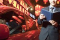 Businessman standing next to his car at night reading, Red lanterns in the background