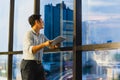 Businessman standing next to office window looking out cityscape with hand holding tablet. Royalty Free Stock Photo