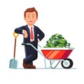 Businessman standing next to wheelbarrow with cash