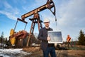 Businessman standing on an oilfield holding mini solar module next to an oil rig Royalty Free Stock Photo