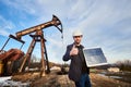 Businessman standing on an oilfield holding mini solar module next to an oil rig Royalty Free Stock Photo