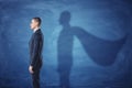 Businessman is standing in profile casting a shadow of the superman`s cape on blue chalkboard background