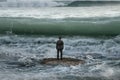 Businessman standing on rock in the ocean facing oncoming waves