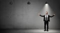 A businessman stands on concrete background under the light of a single working industrial lamp.