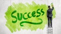 A businessman stands on a stepladder and paints a word Success on a green background with a paint roller. Royalty Free Stock Photo